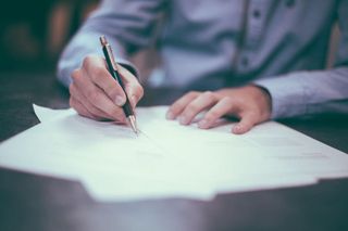 Close-up of a hand signing an official document with a black pen on a wooden desk.